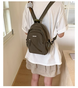 Detail of olive green canvas sling bag with MACHUGE logo and multi-zipper compartments