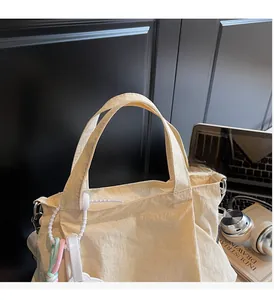 Detail of cream pleated nylon tote bag featuring durable handles and trendy ornaments