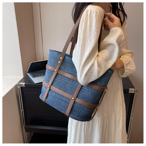 Detail of vintage denim tote bag with brown leather straps and gold metal rivet accents