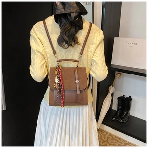 Detail of a dark brown backpack with metal buckle, stylish silk scarf and key pendant