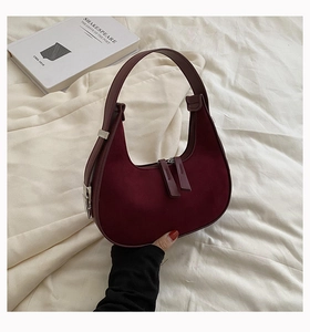 Close-up of burgundy suede crescent underarm bag with double zipper and silver metal buckles