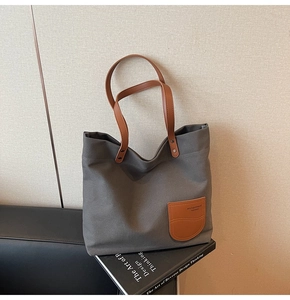 Dettaglio di una borsa tote in tela grigia con manici in pelle marrone e patch logata