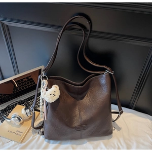 Brown leather tote bag with a white teddy bear charm shown next to a laptop on a desk
