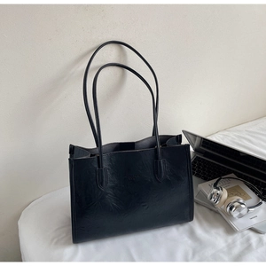 Detail of black tote bag showing leather texture and subtle embossed text for daily use