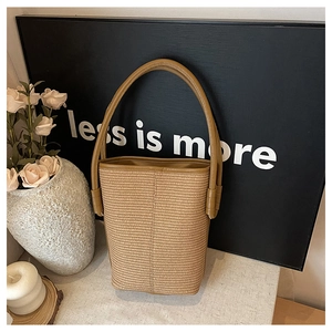 Detailed close-up of the woven texture and brown leather handle on a straw bucket bag