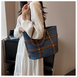 Detail of blue denim tote bag with brown leather straps and gold stud accents