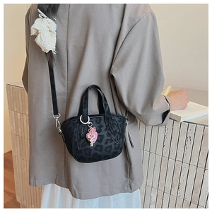 Detail of black leopard print crossbody bag with pink heart charm on casual outfit