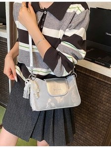 Silver metallic crossbody bag with lace bow and pearl charm worn by a model