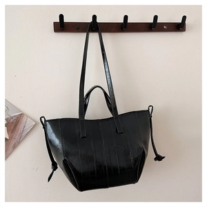 Detail of glossy black leather tote bag featuring drawstring accents and dual straps