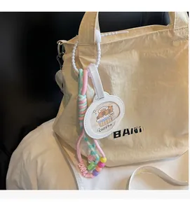 Detail of capybara bag charm with rainbow woven cord and lettered love beads on canvas bag