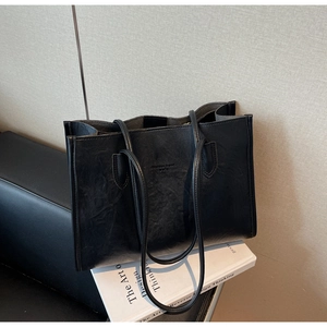 Close-up of black leather tote bag with embossed text on white design books