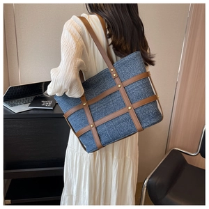 Detail of denim tote bag with brown leather straps and gold rivets shown on model