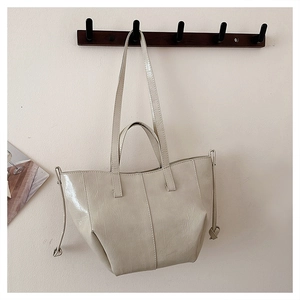 Detailed close-up of cream glossy patent leather tote bag with vertical stitching