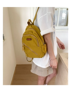 Detail view of mustard yellow nylon backpack with zippers worn on one shoulder by model