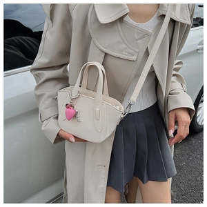 Chic beige crossbody bag with heart charm shown on a model in a beige trench coat