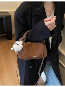 Brown soft leather dumpling bag with white plush monster charm and shoulder strap