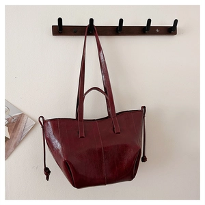 Close-up of a glossy burgundy leather tote bag with stylish side drawstring details