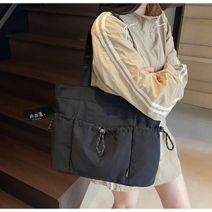 Detail of a large black nylon tote bag featuring a functional drawstring front pocket