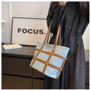 Detail of light blue denim tote bag with brown leather cross straps and vintage rivets