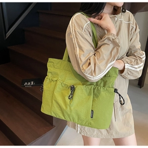 Detail of light green nylon tote bag featuring drawstring outer pockets and woven logo