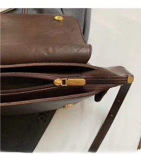 Détail de la fermeture éclair dorée et du fermoir magnétique sur un sac vintage en cuir brun