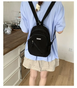 Detail of black mini backpack with silver zipper and MACHUGE label worn by a model