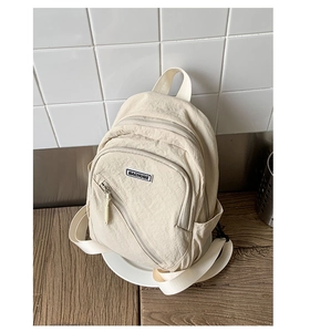 Detail view of the cream nylon chest bag featuring functional zippers and a brand label