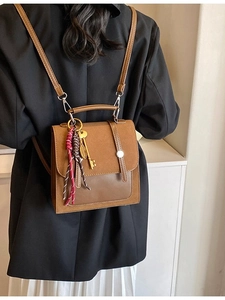 Brown patchwork backpack with suede texture and metal charms worn by model in casual style