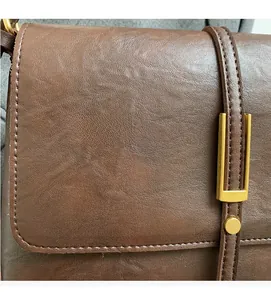 Détail de la texture cuir marron souple avec coutures fines et boucle dorée