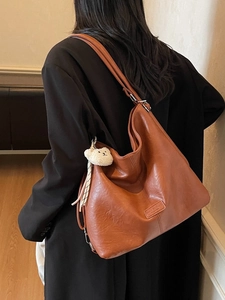 Vintage brown large capacity leather tote bag with plush bear charm worn by a model