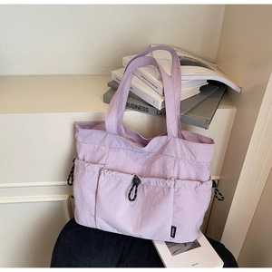 Detail of light purple tote bag featuring multiple exterior pockets and a woven label