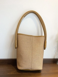 Minimalist woven straw bucket bag with brown leather trim and top handle for beach vacation