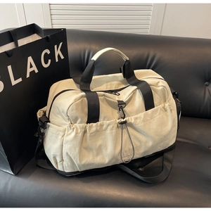 Detail of a beige duffel bag with black straps on a leather sofa showing pockets