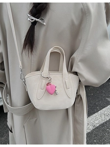Chic beige mini bucket bag with pink heart charm shown on model in trench coat