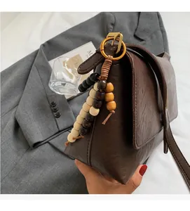 Détail d'un sac bandoulière vintage marron foncé avec charm en perles de bois et rabat