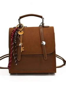 Retro brown patchwork backpack with golden key charm and woven tassels on white background