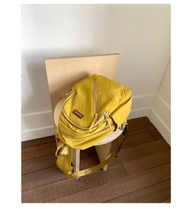 Detail of mustard yellow nylon backpack featuring zipper pockets and brand label on wood chair