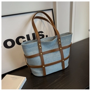 Detailed close-up of blue denim tote bag with brown leather straps and gold rivets