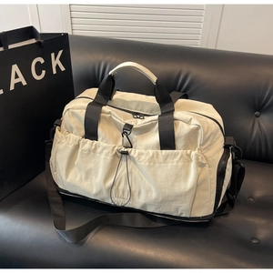 Detail of off-white travel bag with drawstring pocket and black straps on a leather sofa