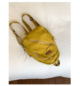 Detail view of mustard yellow nylon backpack with zip pocket and textile brand tag