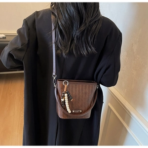 Detail of dark brown woven bucket bag with beaded charm and adjustable strap