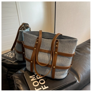 Detail of blue denim tote bag featuring brown leather straps and gold rivet studs