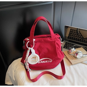 Detail of red nylon tote bag with adjustable strap, brand logo and capybara charm