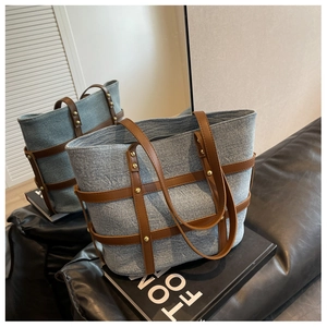 Detail of denim tote bag featuring brown leather straps and gold rivet decorations