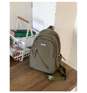 Detailed view of green canvas chest bag with diagonal zipper and side water bottle pocket