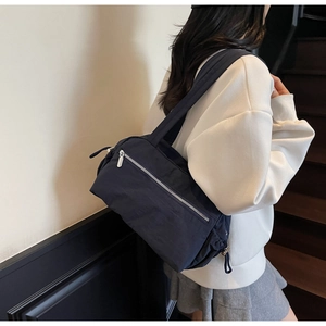 Detail of dark blue lightweight nylon tote bag showing the front zipper pocket and strap