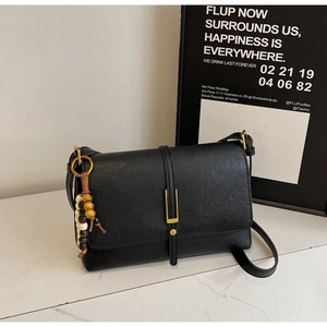 Detail of black matte leather crossbody bag with gold buckle and wooden bead charm