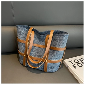 Detailed macro view of denim tote bag with brown leather straps and gold rivets on sofa
