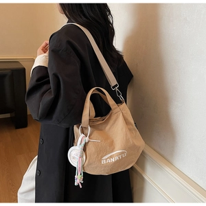 Detail of khaki bucket bag with wide fabric strap and decorative charm on shoulder