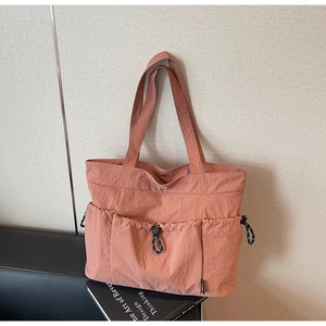 Detail of a large brick red nylon tote bag with three drawstring outer pockets on a black seat